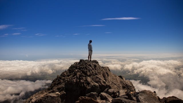 A man stands on the top of a mountain overlooking clouds