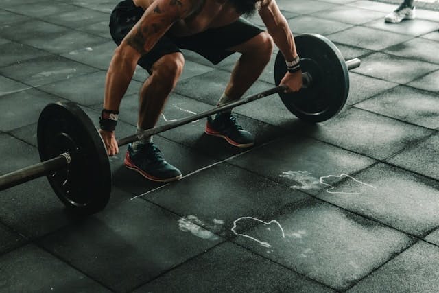 A man in workout shorts deadlifting a barbell with two 45 lb plates.
